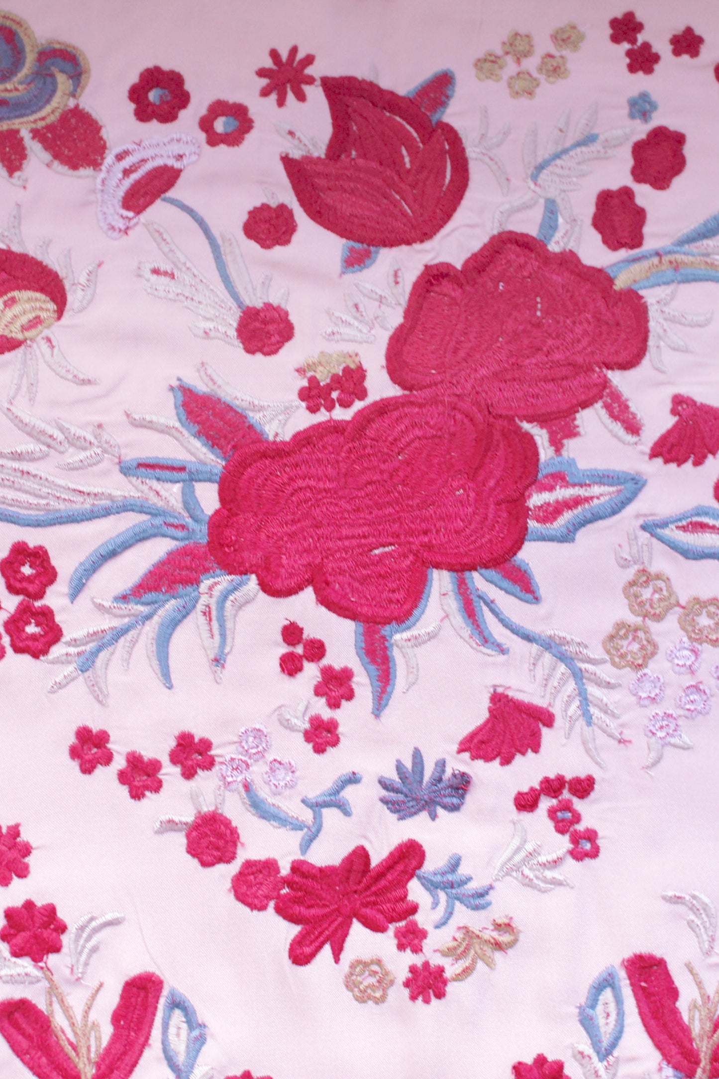 Descubre el manton Noa en rosa con diseño floral rojo. Confeccionado en algodón y flecos de seda, es una pieza artesanal única para tu look flamenco.