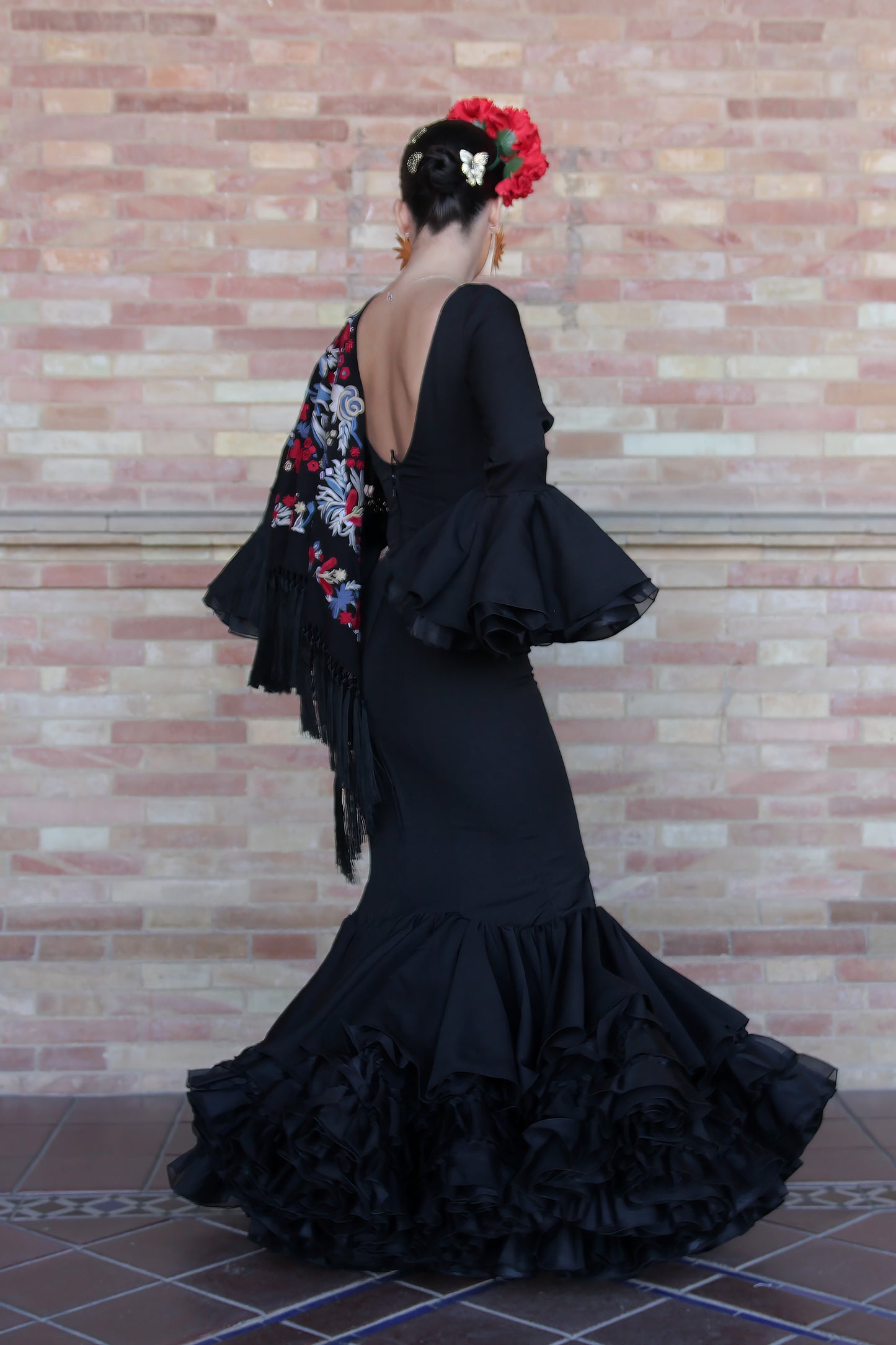 El vestido de flamenca negro Clavel con mantón y complementos, incluyendo el ramillete Rojo Pasión y pendientes dorados Hinojos, es el conjunto perfecto para brillar en la Feria de Abril con estilo y sofisticación.