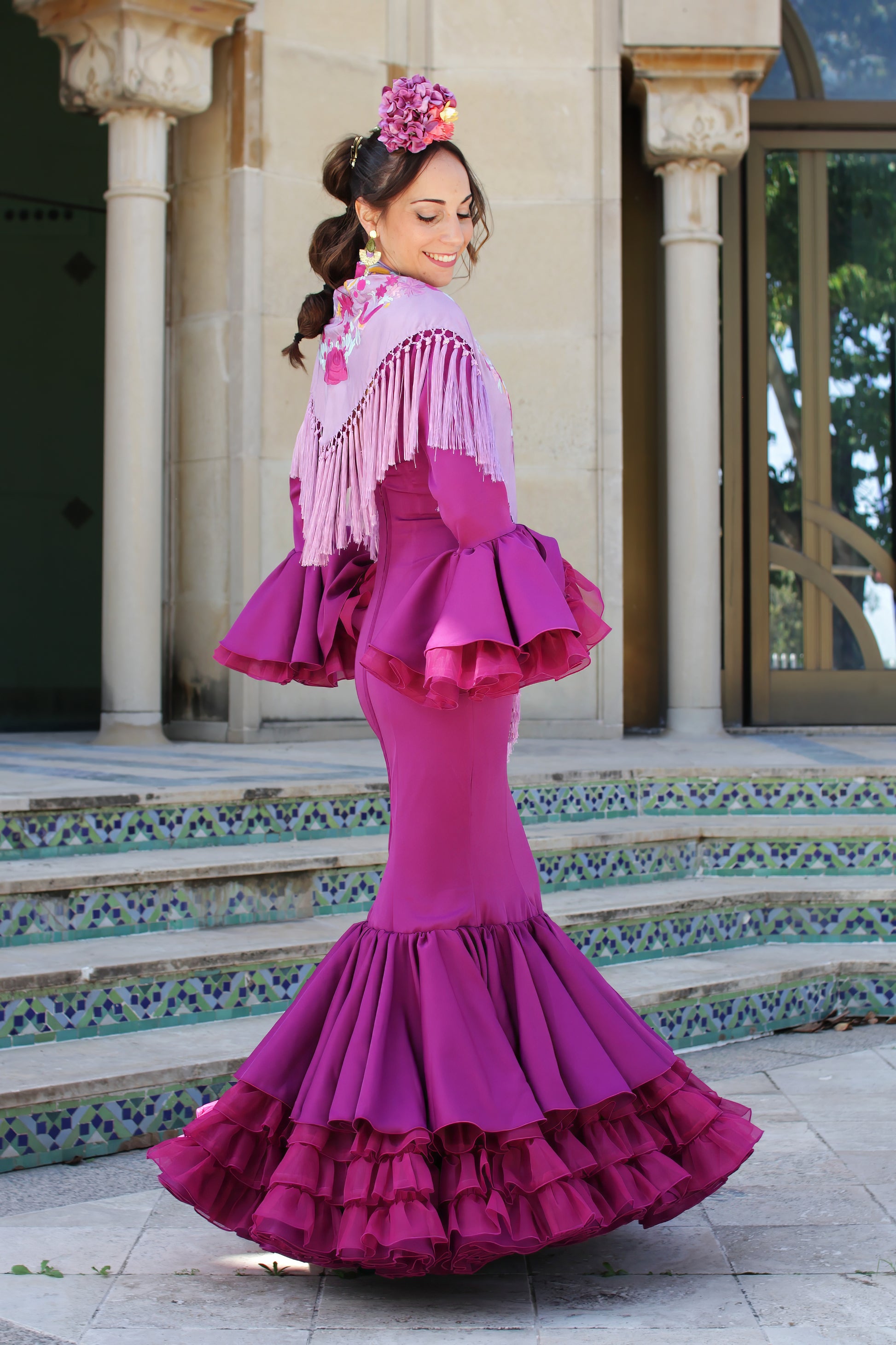 El Look para Feria de Abril perfecto. Traje de flamenca buganvilla combinado con mantón buganvilla, ramillete Jaleo y pendientes dorados Nerja. Una combinación ideal de estilo y tradición flamenca para destacar con fuerza.