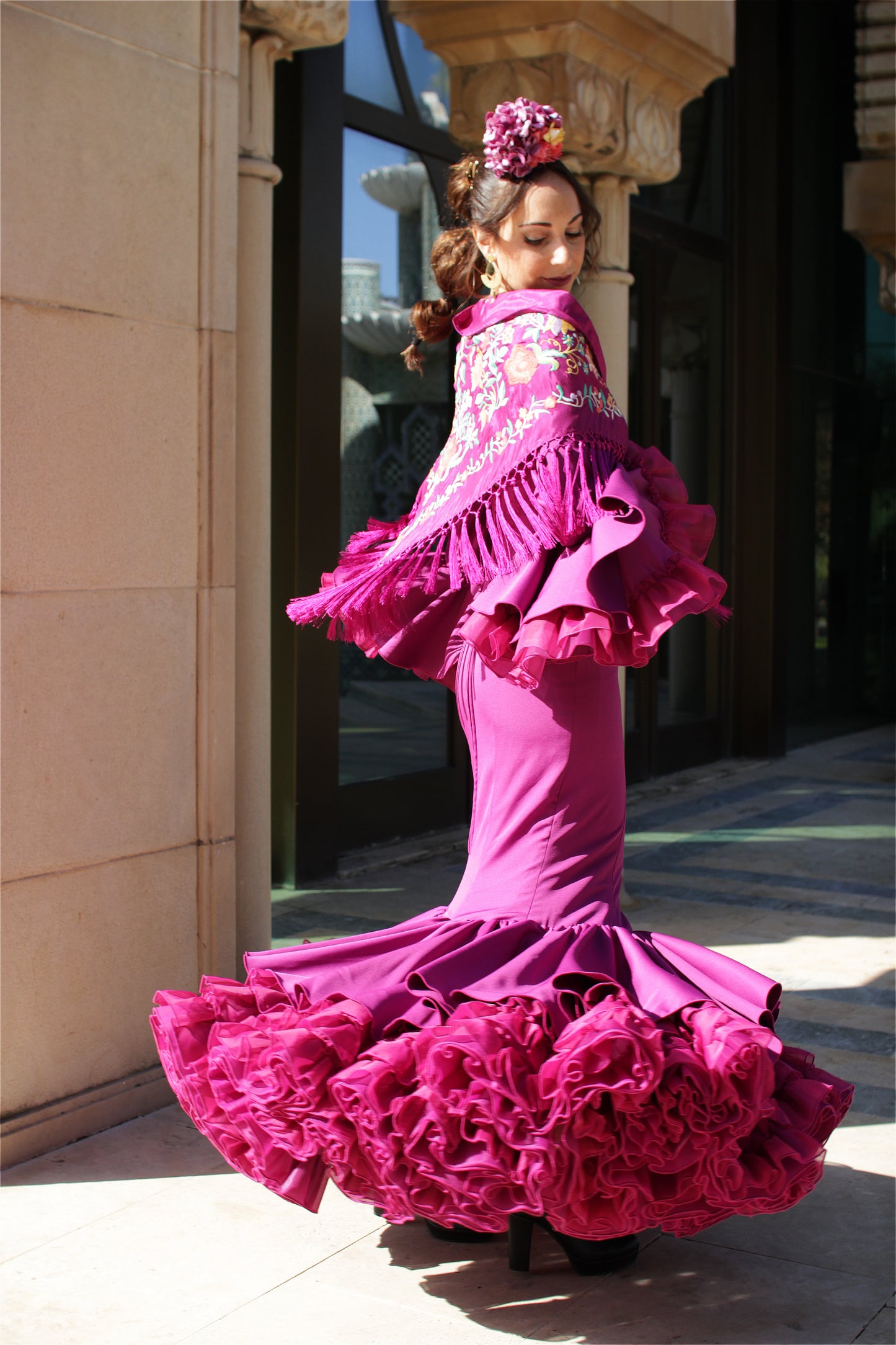 Cautiva en la Feria de Abril con este conjunto flamenco. El traje de flamenca buganvilla se acompaña de un mantón lila con flor buganvilla y amarillo, ramillete Jaleo y pendientes dorados Nerja, para un look lleno de luz y color.
