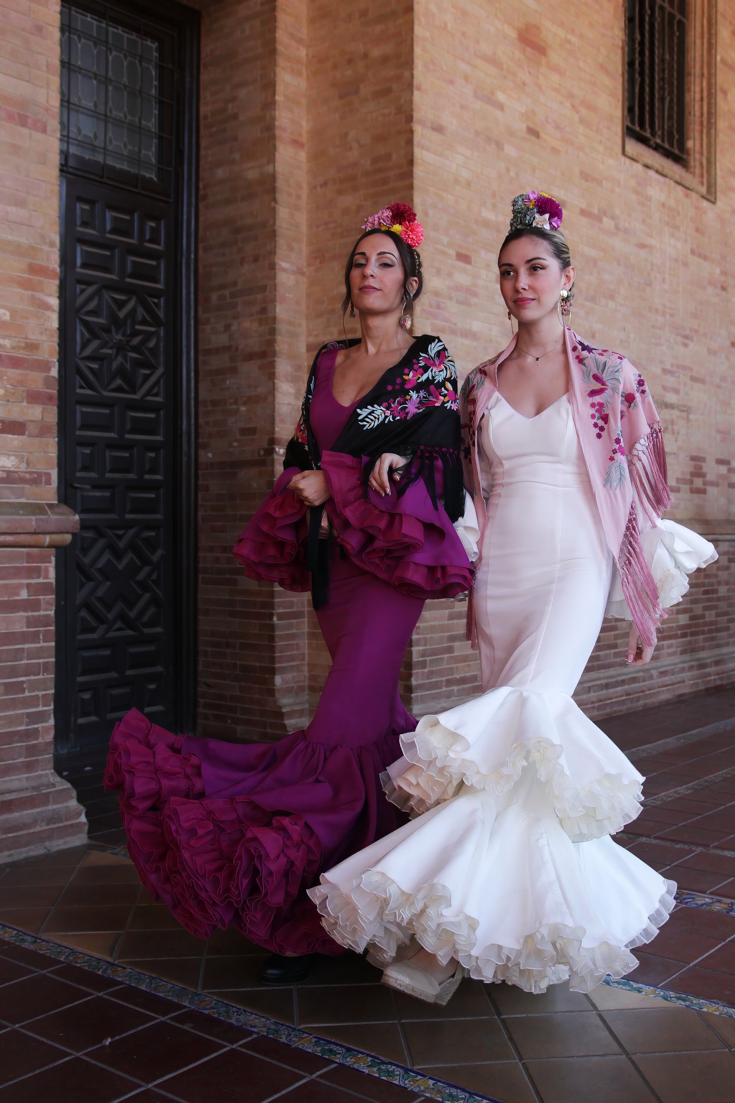 Luce la elegancia del traje de flamenca marfil Jazmin, acompañado de un manton rosa con flor buganvilla, ramillete Duende y pendientes dorados Jara, para un look flamenco sofisticado y lleno de personalidad.
