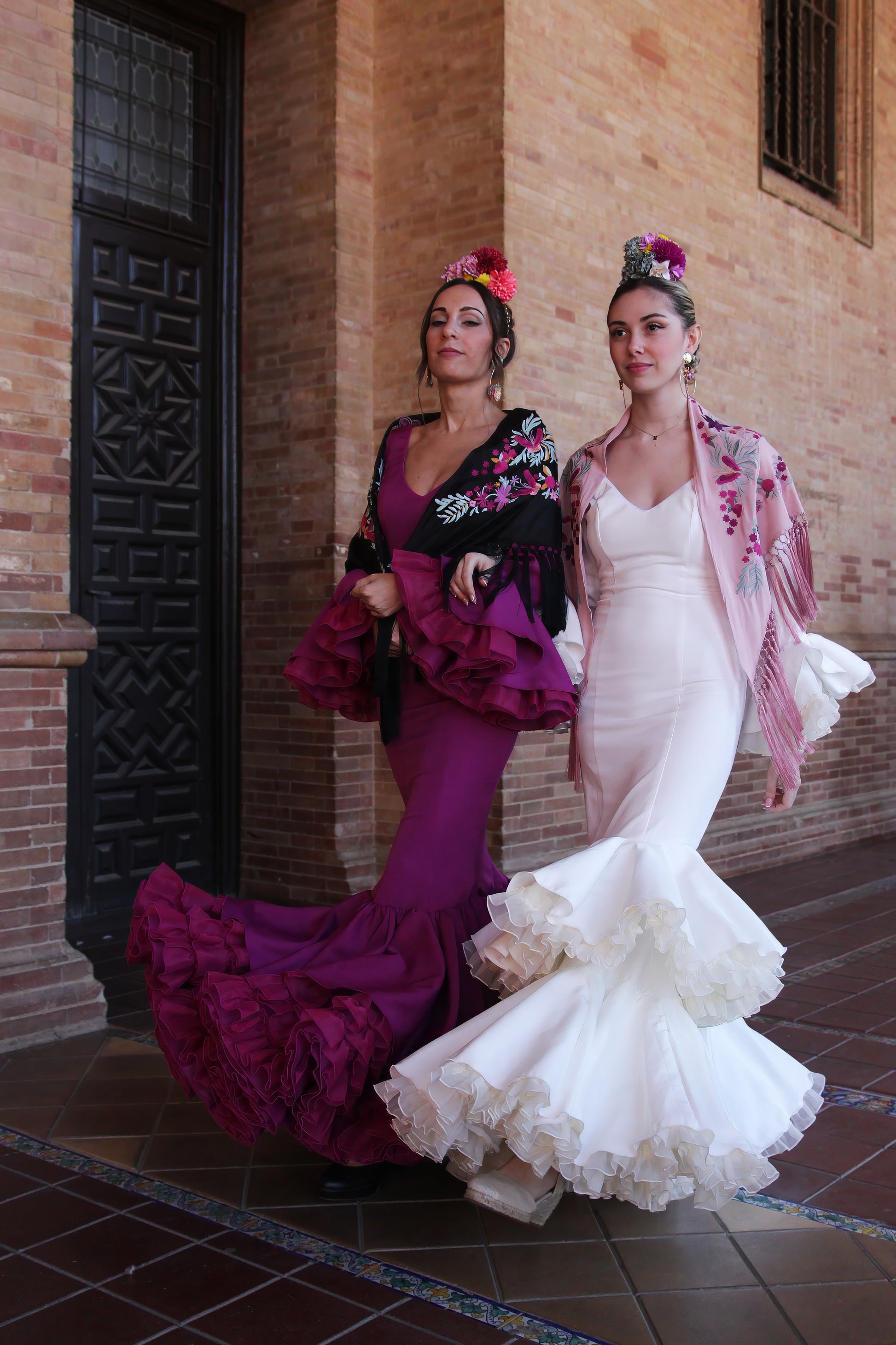 Luce la elegancia del traje de flamenca marfil Jazmin, acompañado de un manton rosa con flor buganvilla, ramillete Duende y pendientes dorados Jara, para un look flamenco sofisticado y lleno de personalidad.