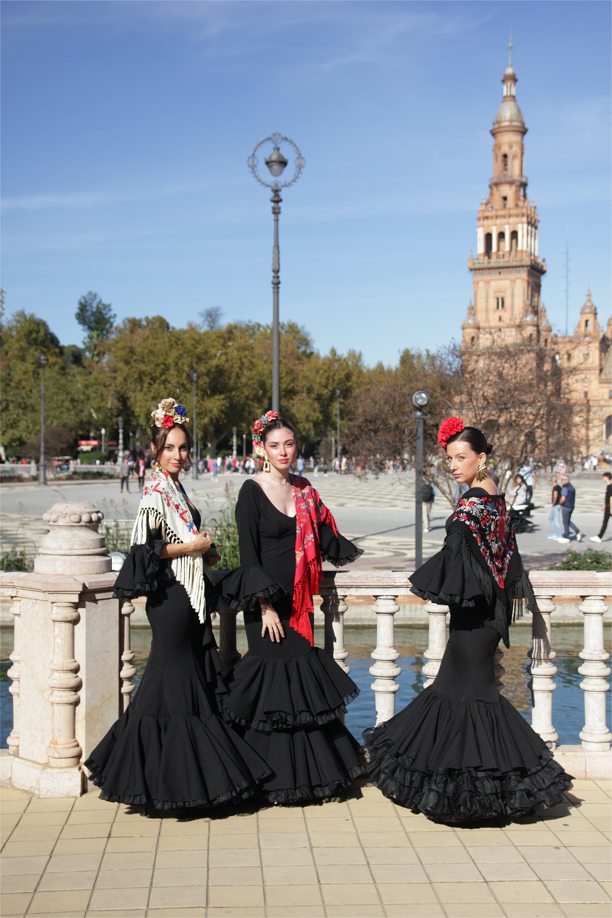 Luce radiante con el vestido de flamenca negro Clavel, a juego con el mantón negro y flor roja, el ramillete Rojo Pasión y los pendientes dorados Hinojos. Un look completo para brillar en la Feria de Abril.