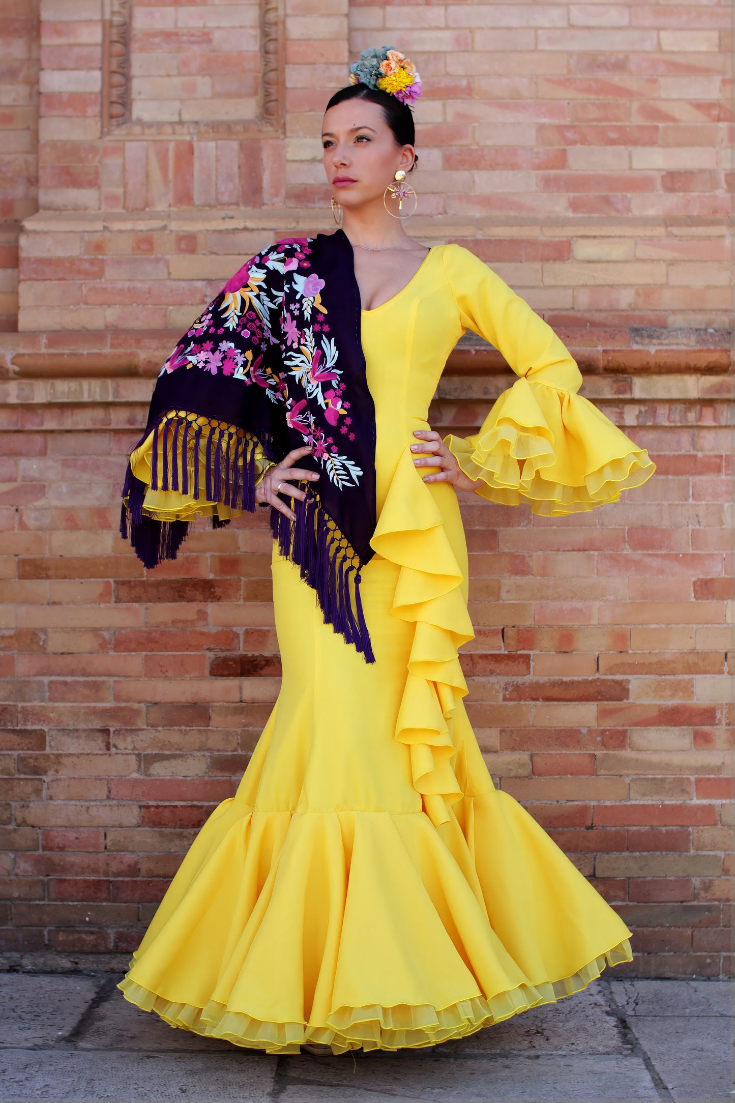 Conjunto perfecto para la Feria de Abril: vestido de flamenca amarillo Azahar, mantón morado con detalles en buganvilla y amarillo, ramillete de flores Brisa y pendientes dorados Jara. Un look radiante para esta temporada flamenca.