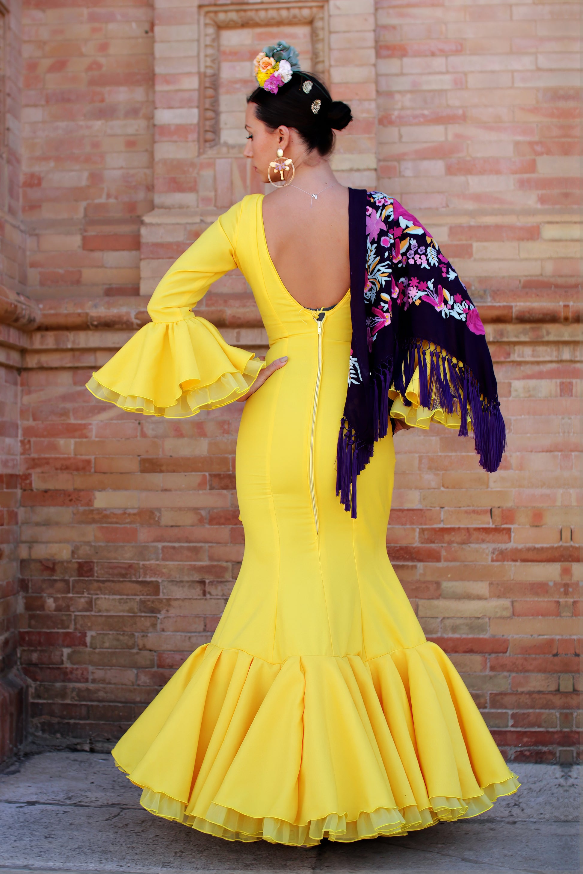 Viste para impresionar en la Feria de Abril con el traje de flamenca amarillo Azahar, mantón morado con patrón buganvilla, ramillete Brisa y pendientes dorados Jara. Conjunto elegante y vibrante.