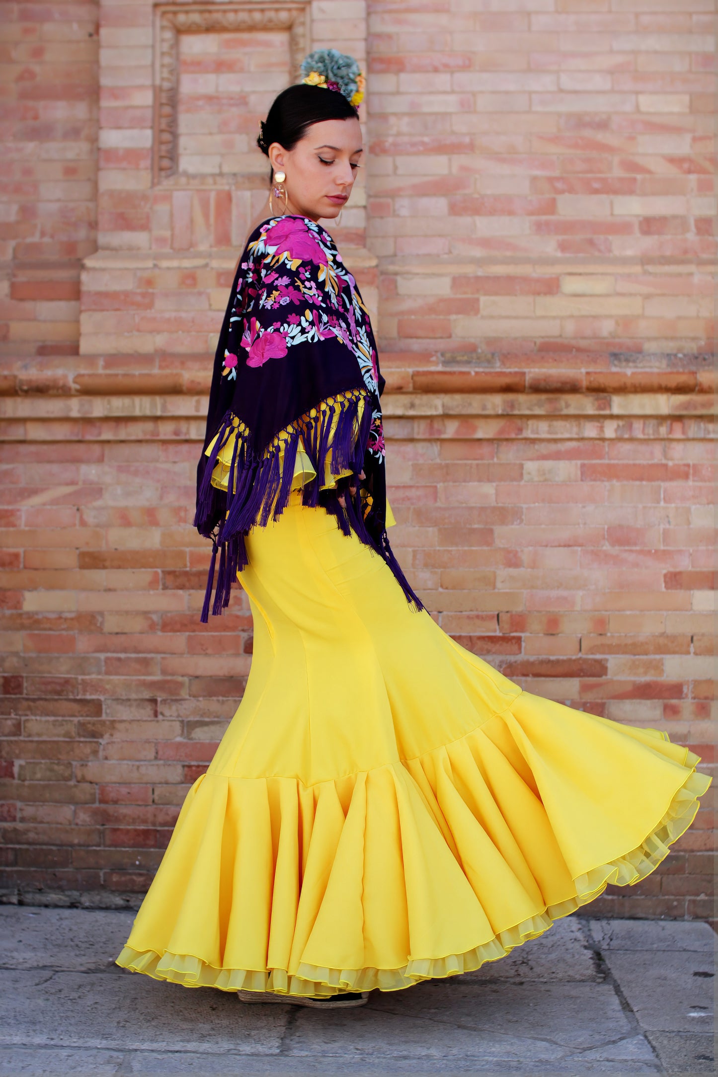Completa tu look para la Feria con el vestido de flamenca amarillo Azahar, mantón morado con patrón buganvilla, ramillete Brisa y pendientes dorados Jara. Conjunto perfecto para brillar en la feria.