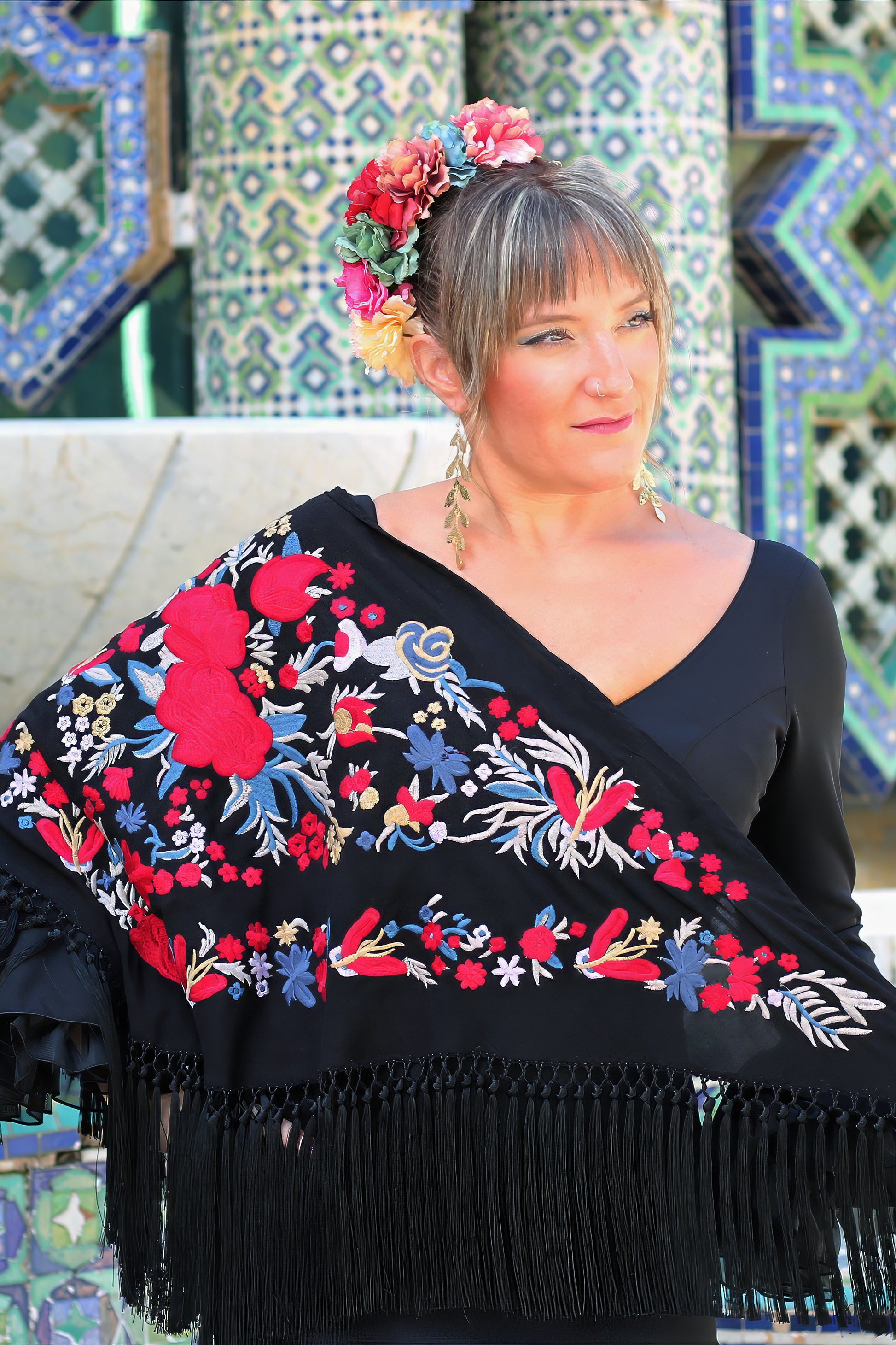Completa tu outfit flamenco con el manton negro Noa. Su diseño floral en rojo y azul aporta elegancia y originalidad a tu look.