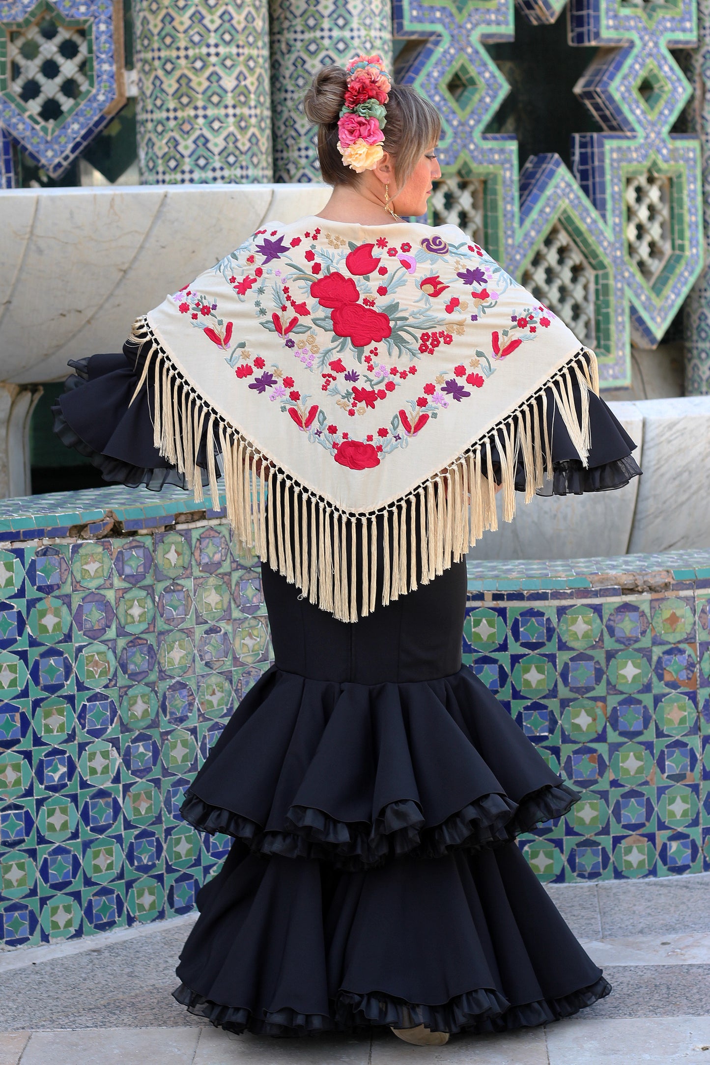 El manton beige Noa con flor roja y morada aporta elegancia y un toque moderno a tu look flamenco. Ideal para la feria.