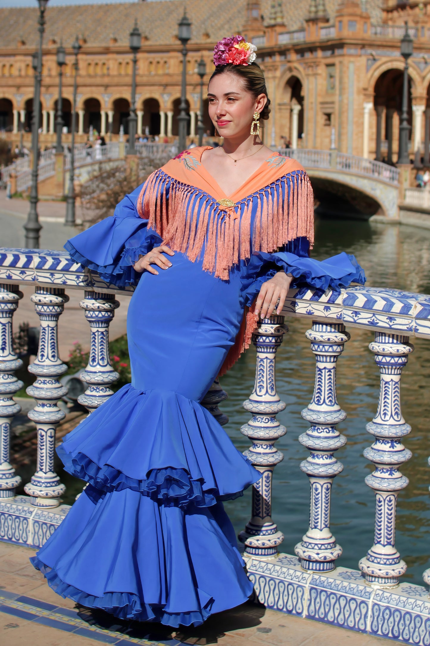 Completa tu traje de flamenca con el manton Noa. Su color mandarina y flores buganvilla, confeccionado en algodón con flecos de seda, lo hacen único y especial.