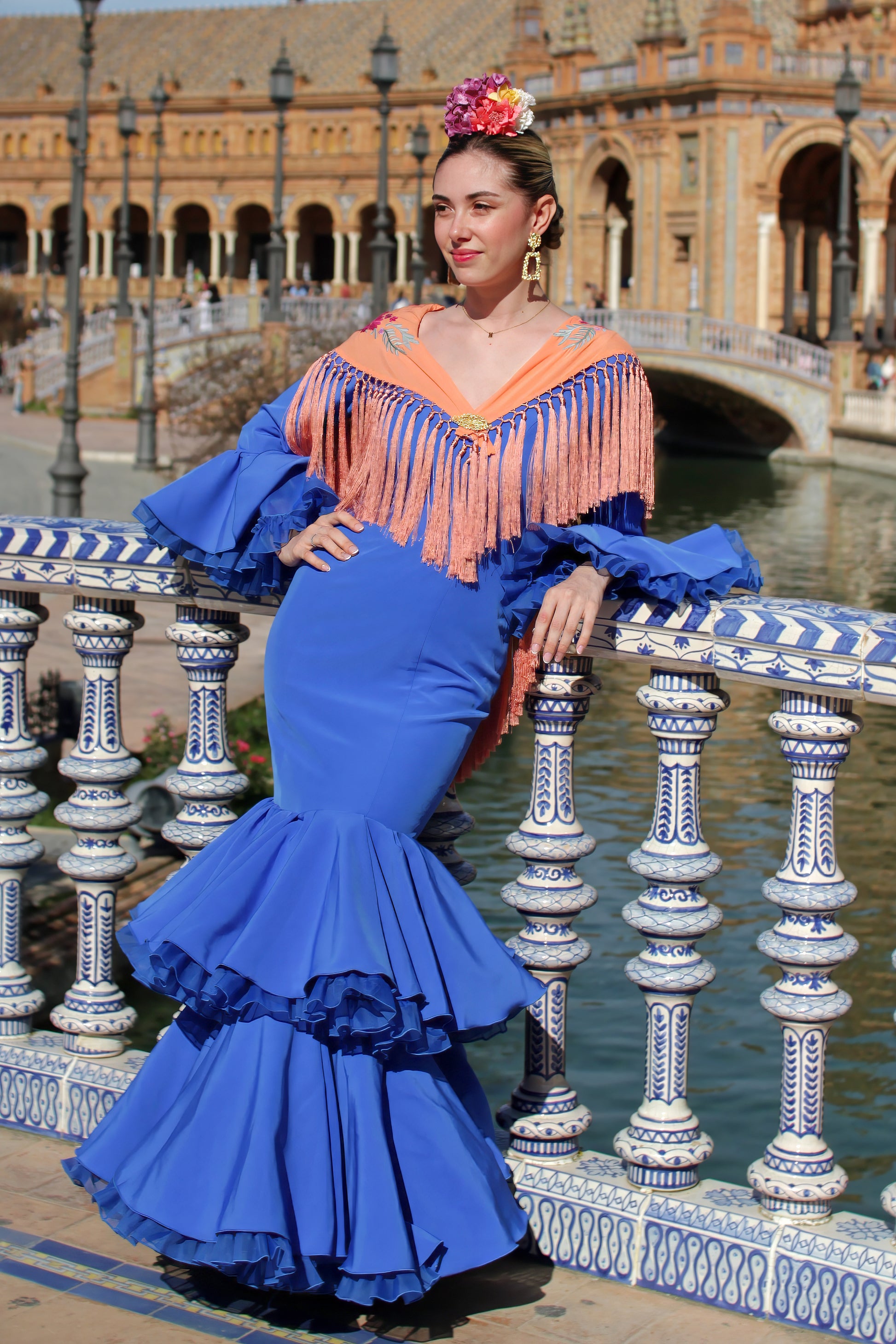 Completa tu traje de flamenca con el manton Noa. Su color mandarina y flores buganvilla, confeccionado en algodón con flecos de seda, lo hacen único y especial.