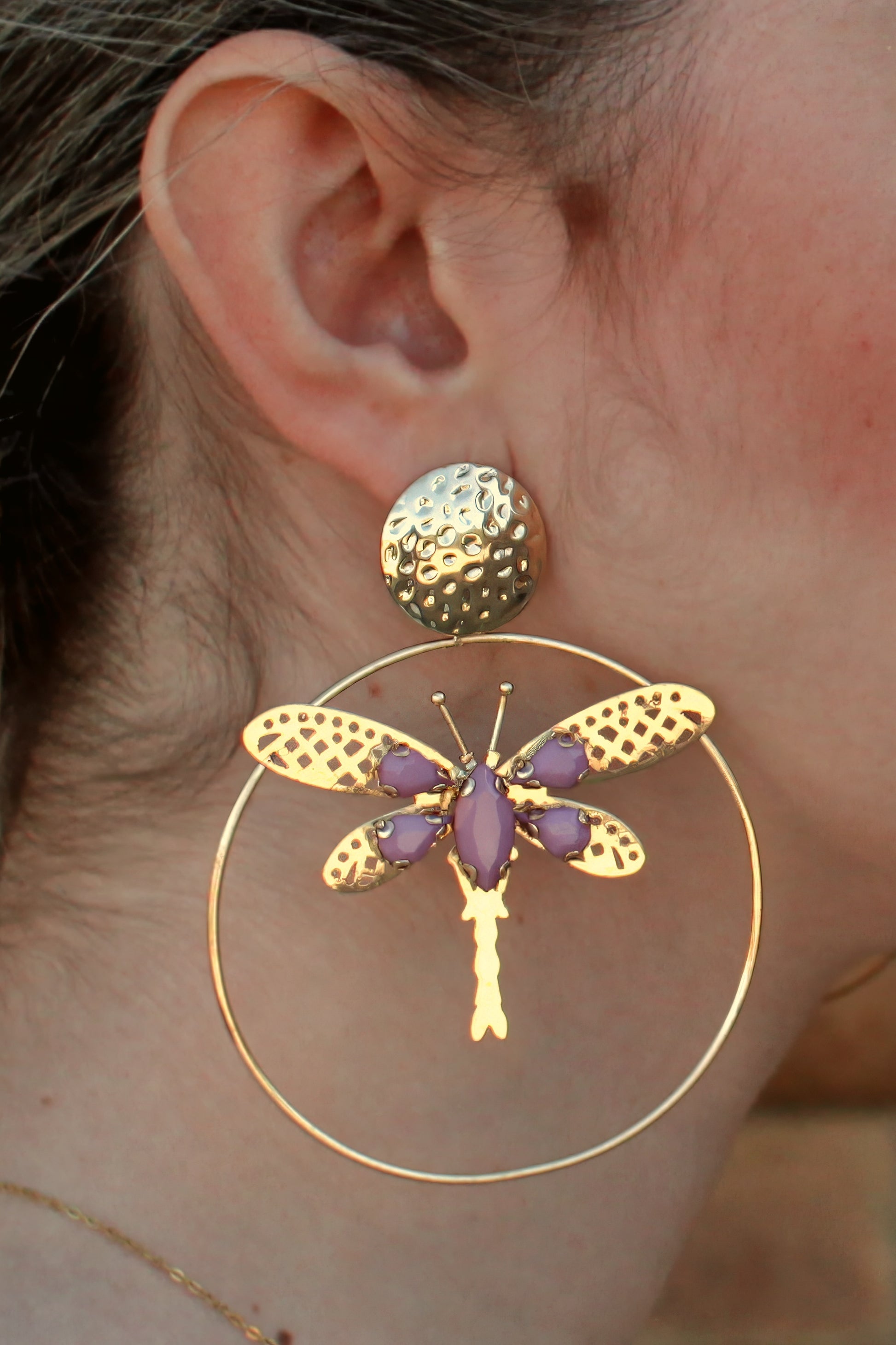 Los pendientes Jara combinan la elegancia del aro dorado con una libélula dorada decorada con detalles malva. Un accesorio único y sofisticado para añadir frescura y delicadeza a tu look flamenco.