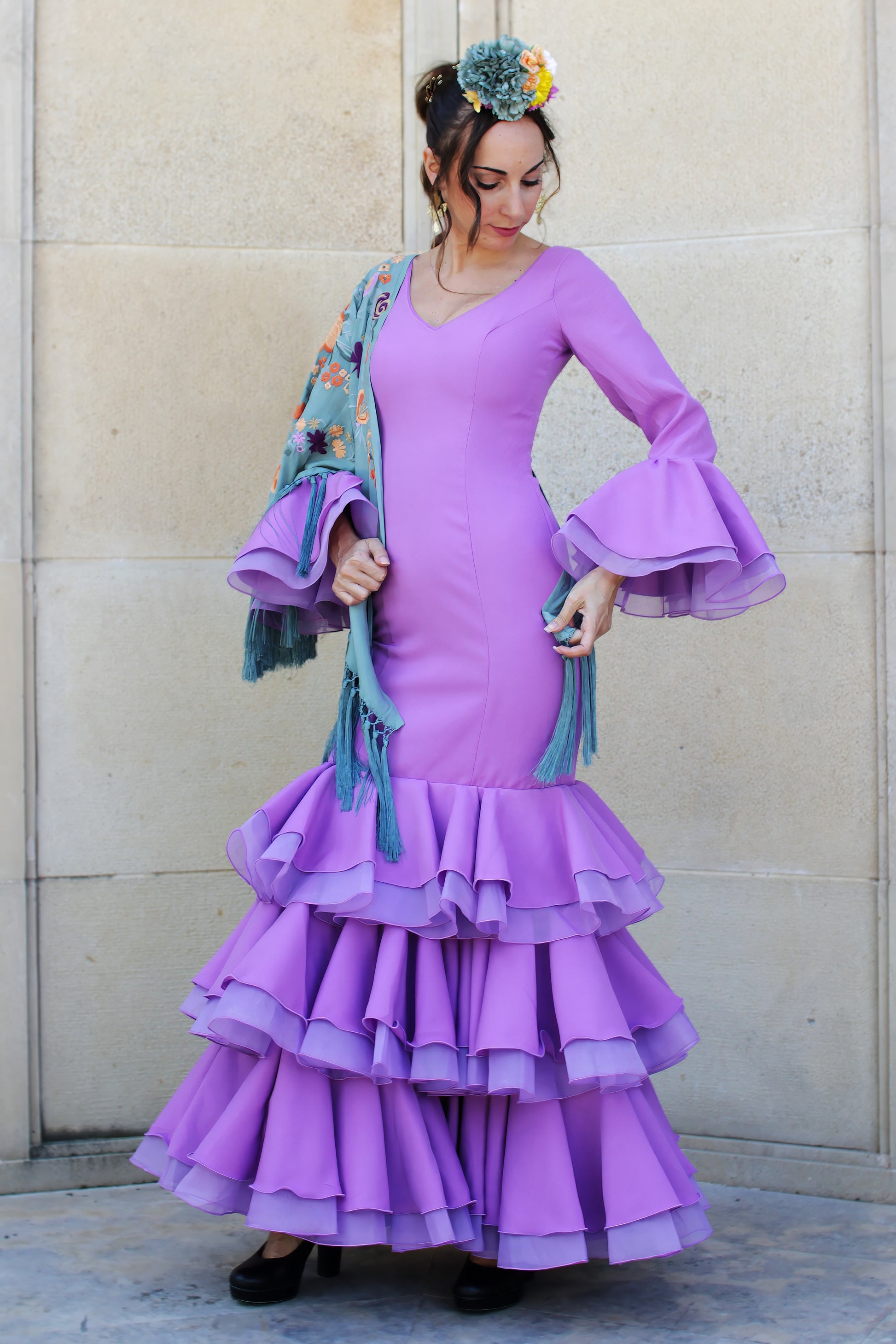 Traje de flamenca Lavanda en color lila, con pendientes flamenca dorados, ramillete de flores y mantón de flamenca, diseñado para la Feria de Abril.